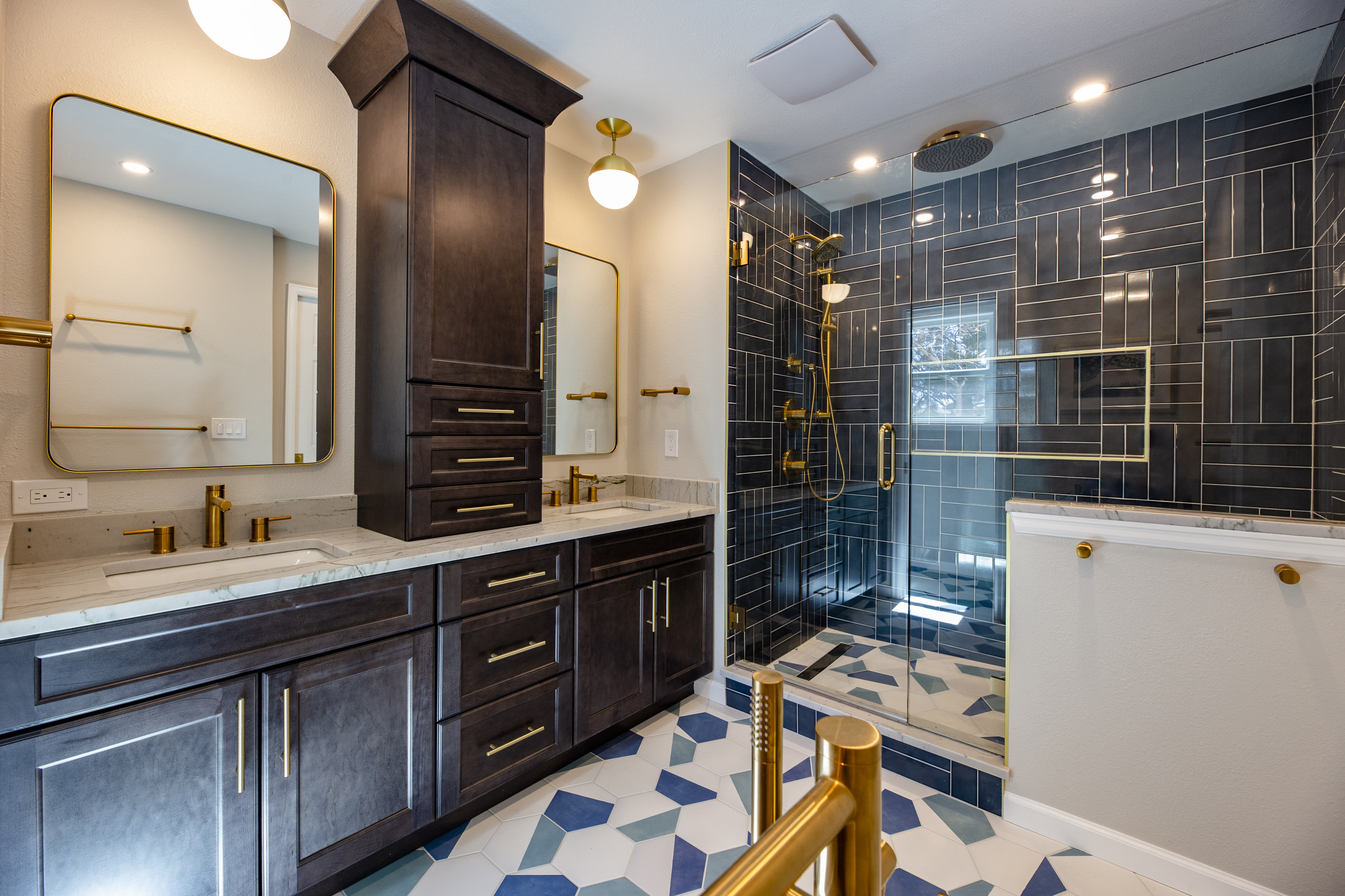Luxurious bathroom with dark wood vanity, gold fixtures, and a glass shower featuring dark blue tiled walls.