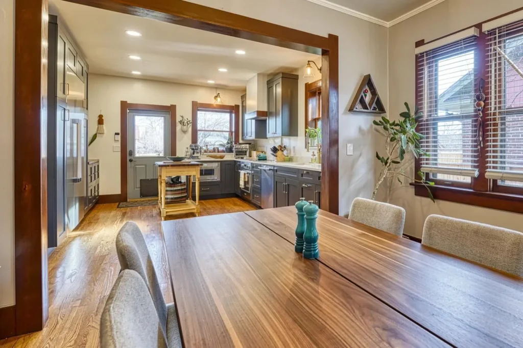 View from a walnut dining table into a remodeled kitchen with dark cabinets and wood floors