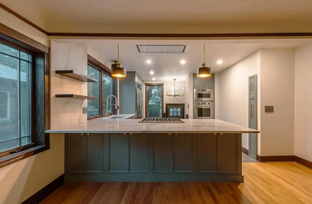 Sage green peninsula with a marble top, floating shelves, and oak floors in an open kitchen