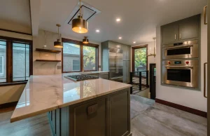 Kitchen with sage green cabinets, a marble island, stacked wall ovens, and brass pendant lights