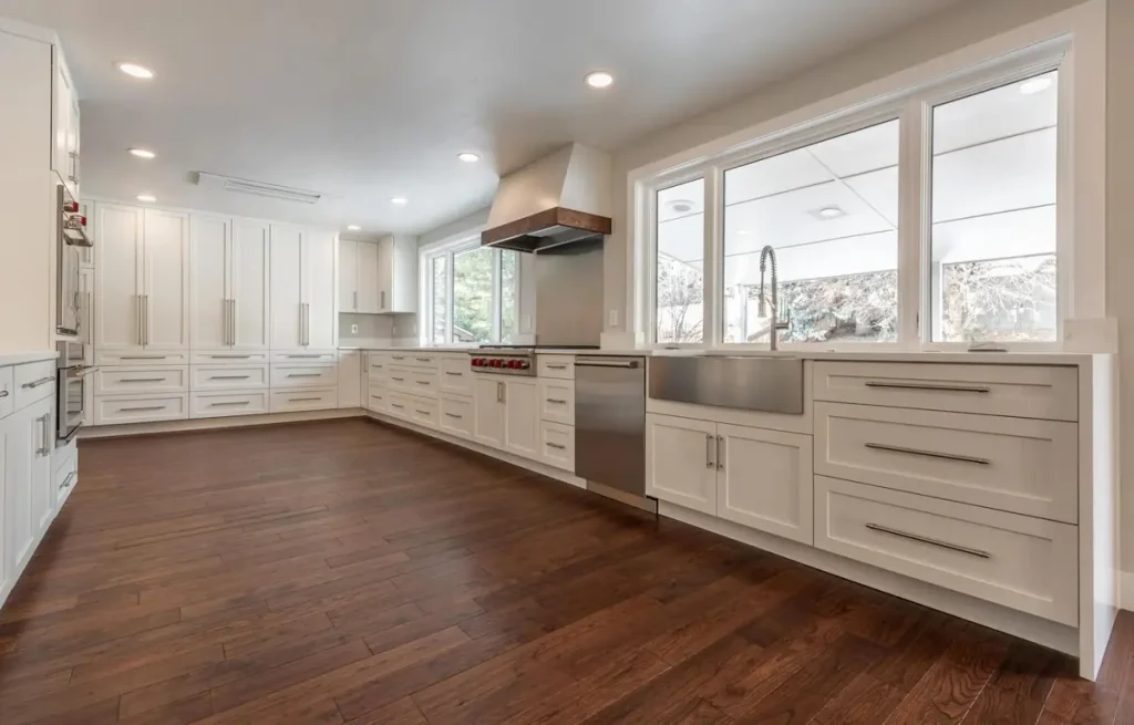 White kitchen with tall cabinets, a farmhouse sink, a wide window, and dark wood floors